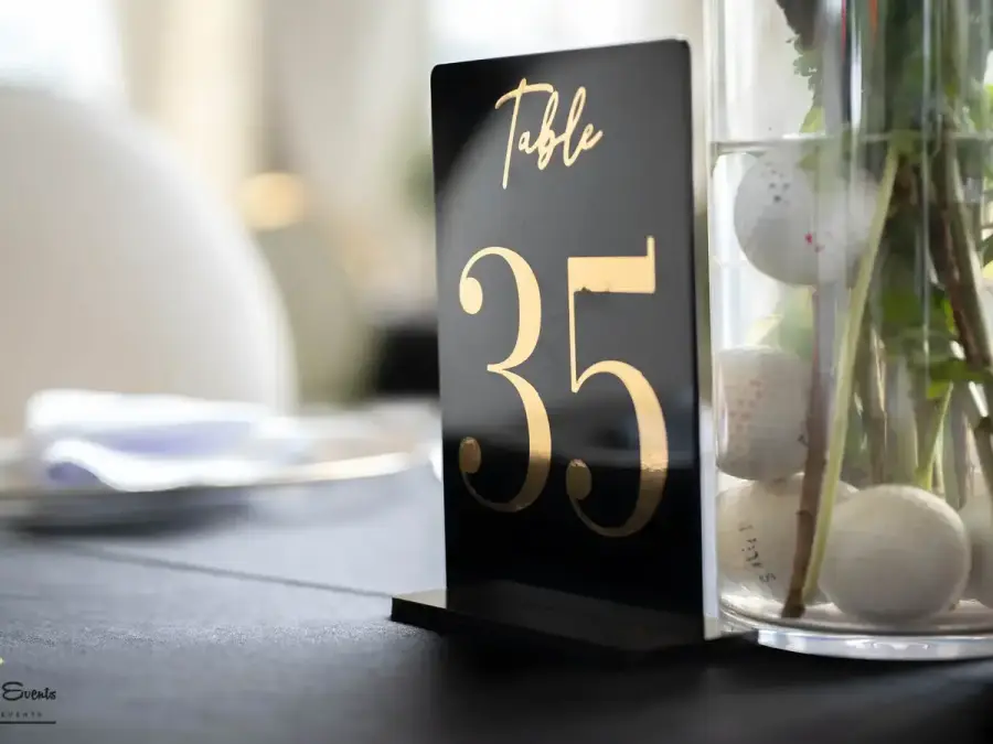 Close-up of a black and gold acrylic table number "35" on a black tablecloth, next to a