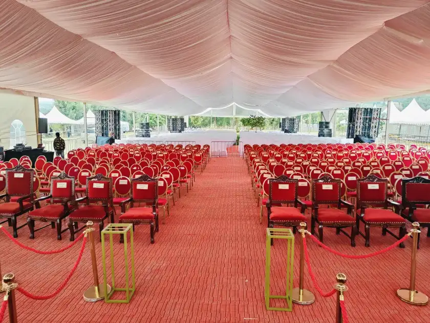 Large white tent interior with a red carpet aisle and rows of red banquet chairs.