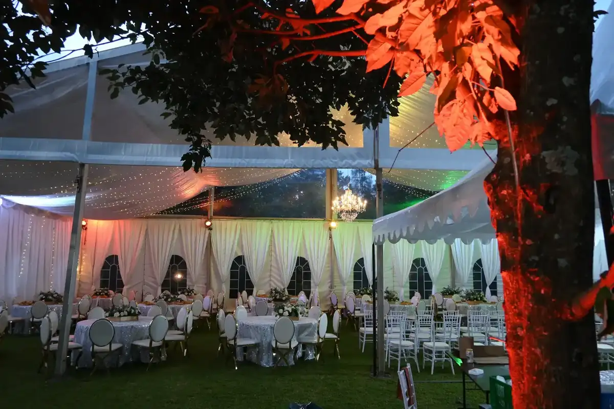 Evening shot of a clear-roof marquee tent with fairy lights and chandeliers, featuring red