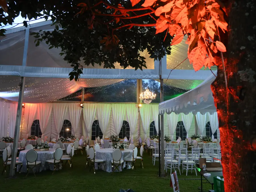 Evening shot of a clear-roof marquee tent with fairy lights and chandeliers, featuring red uplighting and round tables with white linens.