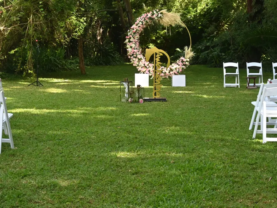 Outdoor garden wedding ceremony setup with white folding chairs facing a large circular floral arch capable of hosting signage.
