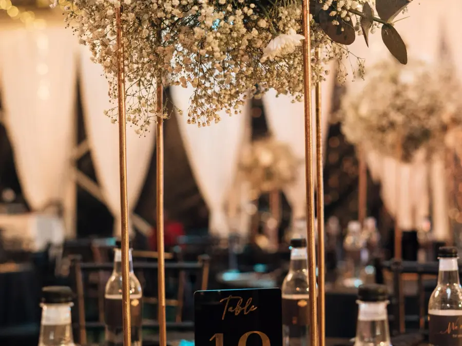 Tall gold geometric centerpiece stand topped with a large arrangement of baby's breath, placed on a table with number 18.