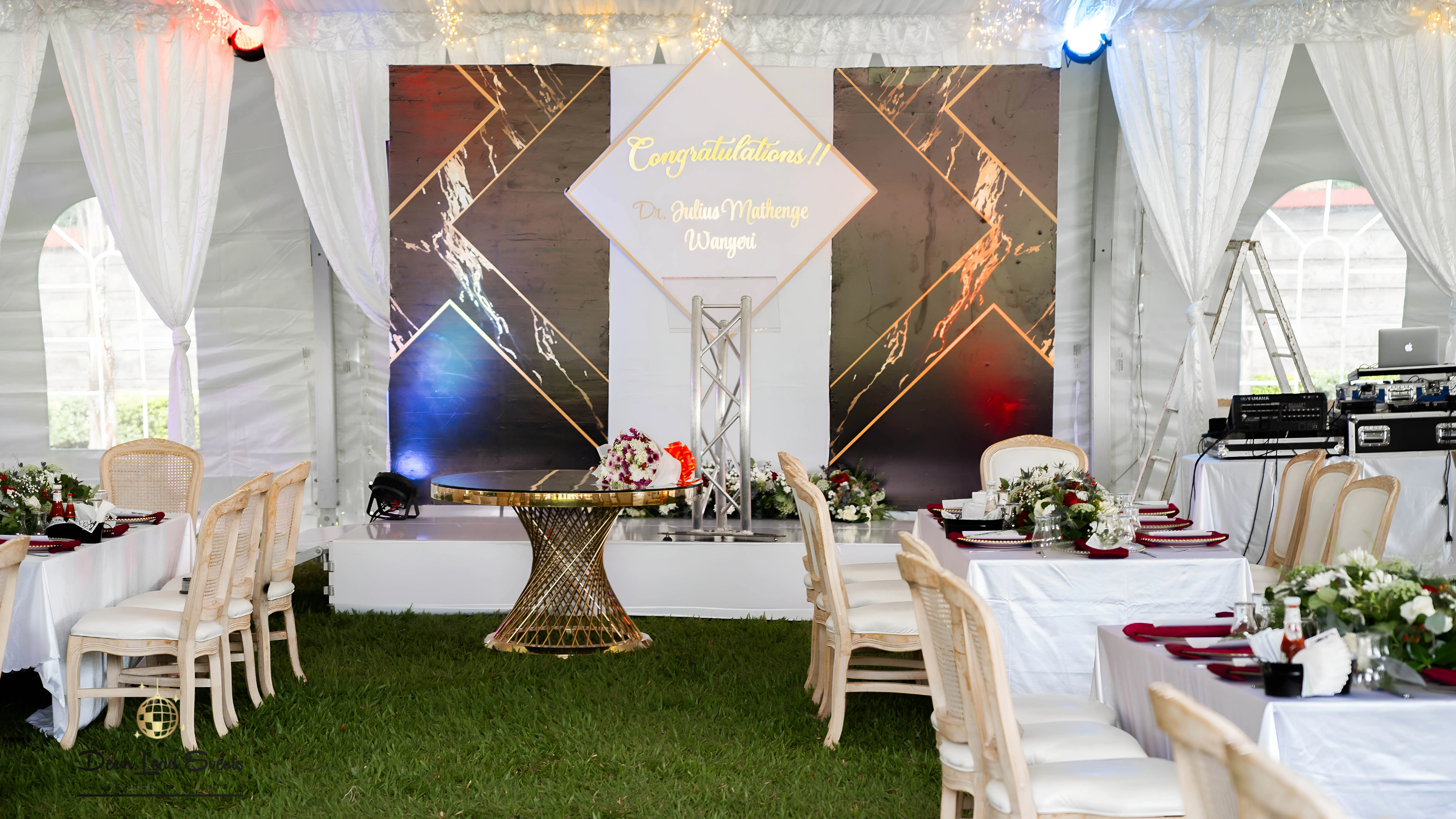Graduation party stage setup with a black and gold backdrop reading "Congratulations Dr. Julius Mathenge Wanyiri" and gold furniture.