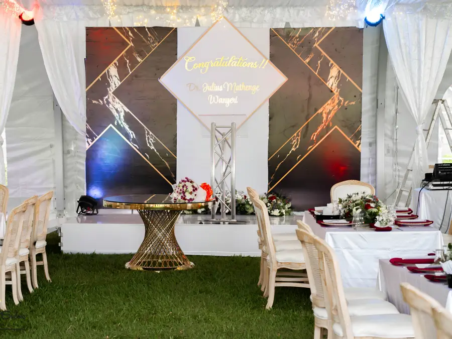Graduation party stage setup with a black and gold backdrop reading "Congratulations Dr. Julius Mathenge Wanyiri" and gold furniture.