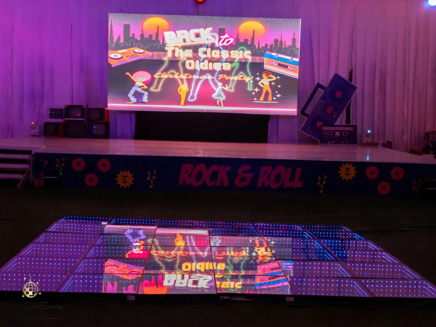 View of a "Back to the Classic Oldies" themed stage with an illuminated LED dance floor reflecting the retro graphics on screen.