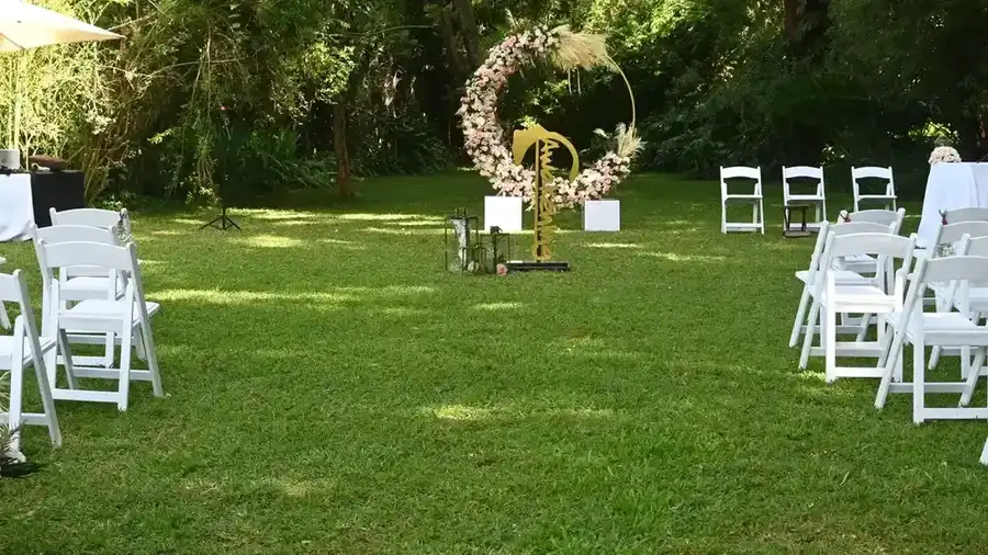 Outdoor garden wedding ceremony setup with white folding chairs facing a large circular floral arch