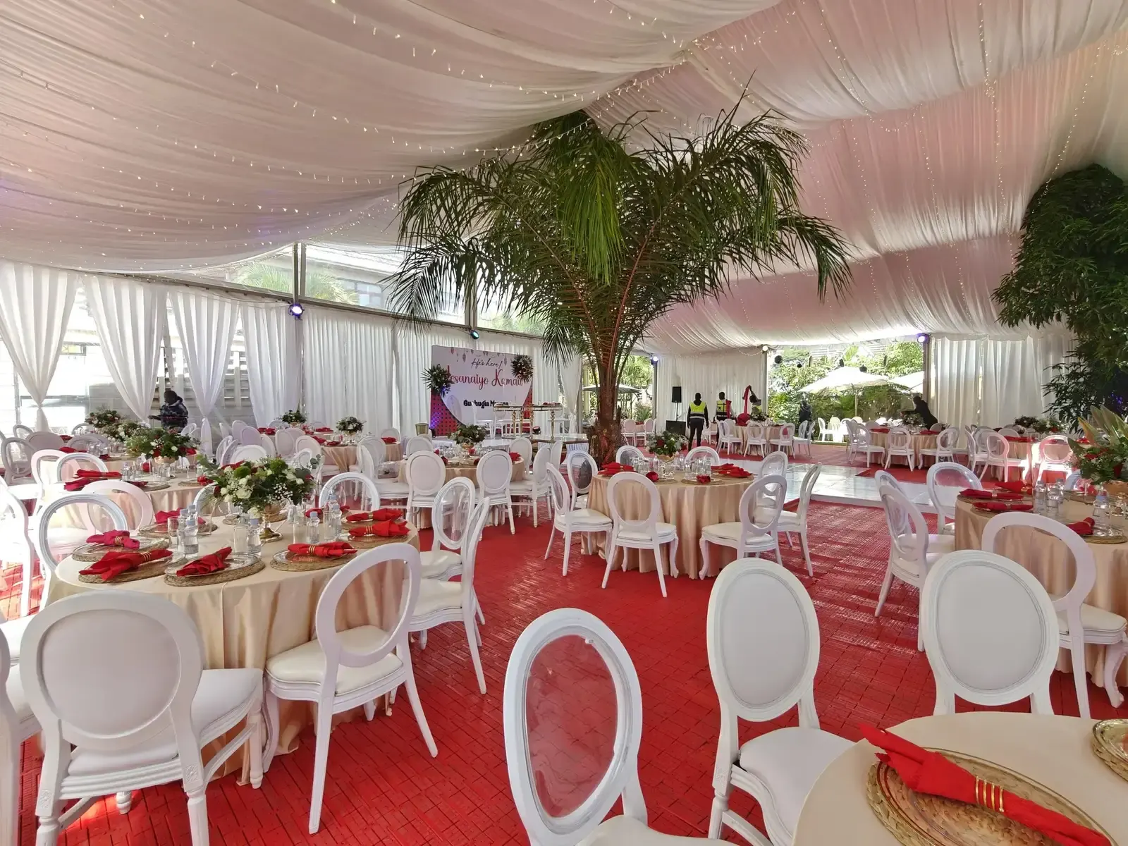 Event tent setup with draped ceiling, red aisle, and round tables
