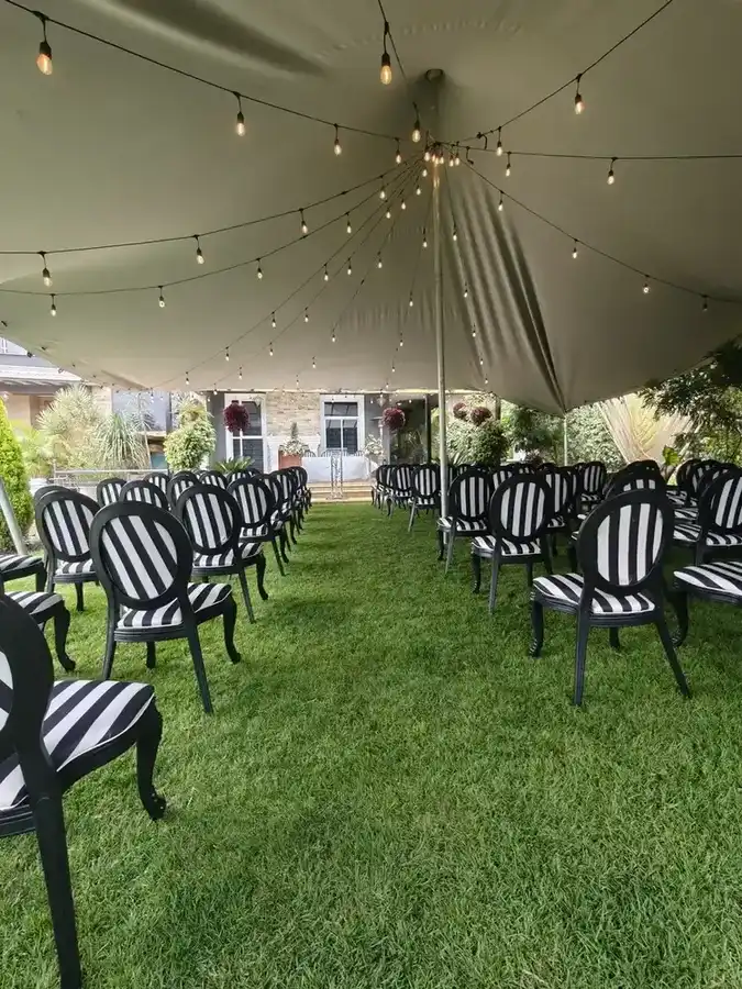 Outdoor ceremony setup on a green lawn with black and white striped Louis chairs arranged in rows