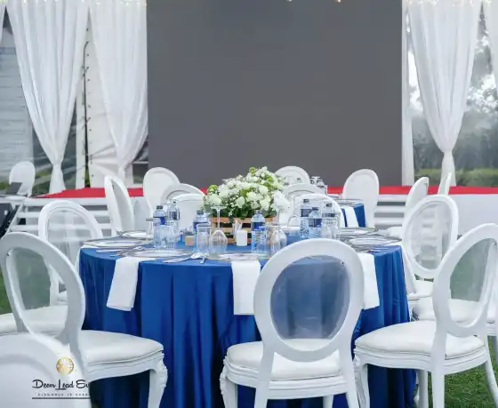 Close-up of a table setting with blue linen, white Louis chairs, and a white floral centerpiece in