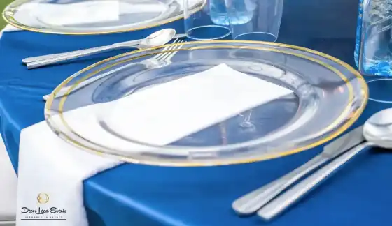 Close-up of a table setting featuring a gold-rimmed clear glass plate, white napkin, and cutlery on
